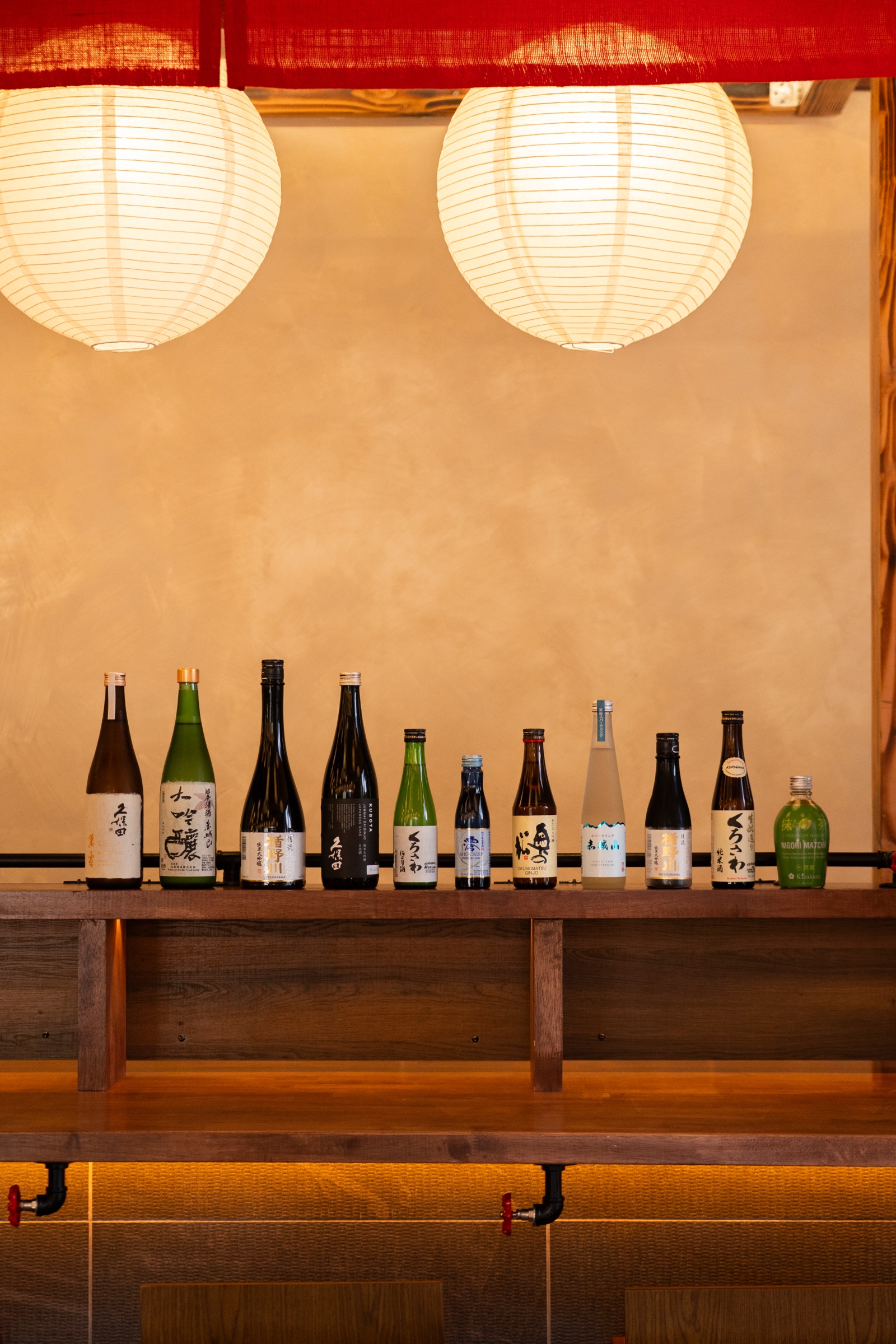 Curated sake bottles lined along the bar under paper lanterns