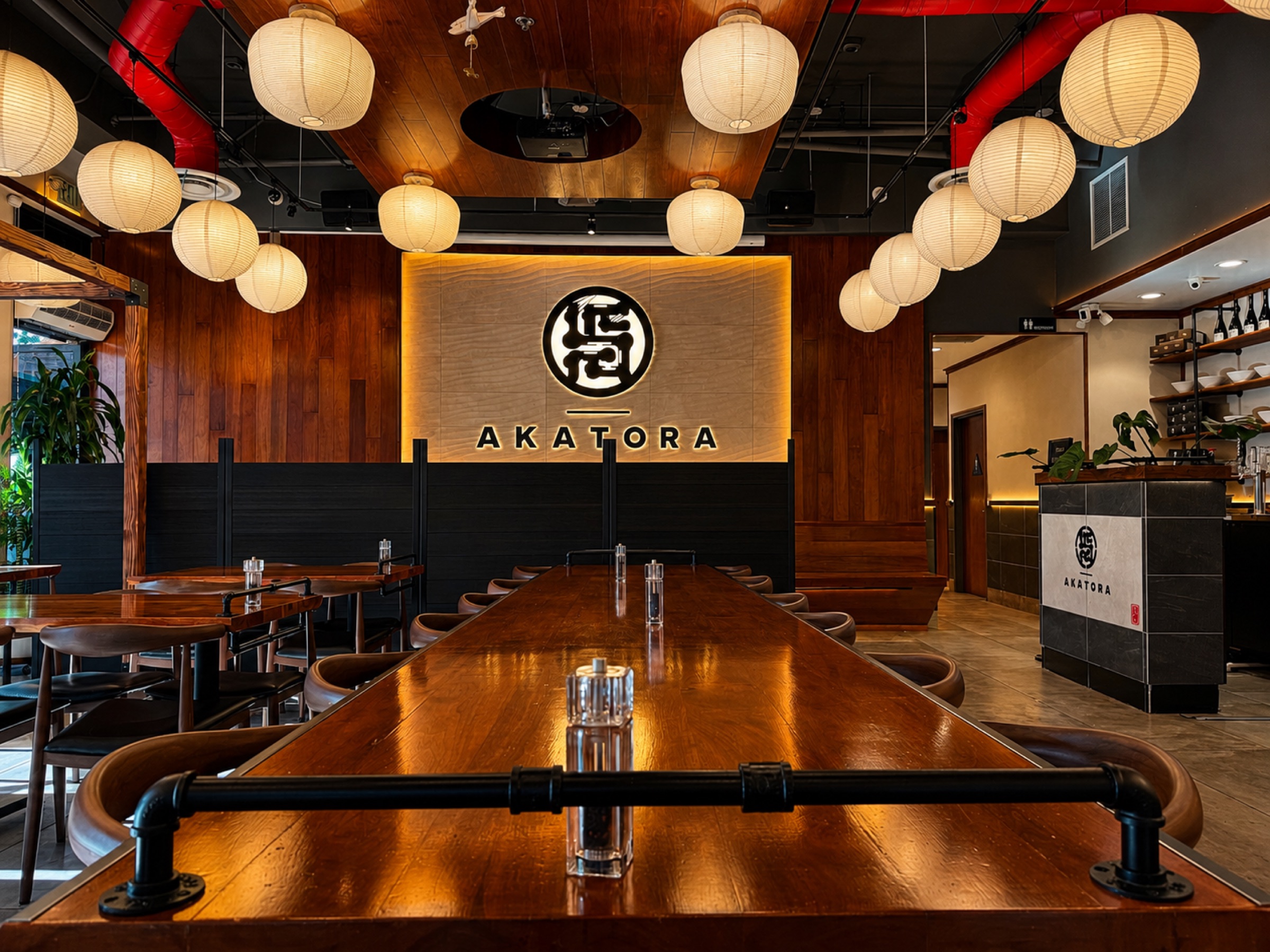 Communal dining table beneath warm paper lanterns at Akatora